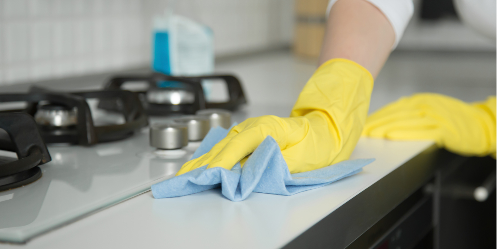Cleaning kitchen countertop and cooker panel with rubber yellow gloves