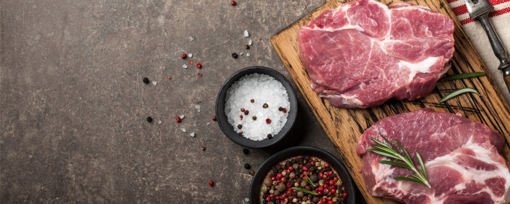 Raw red meat on wooden chopping board with rosemary garnishing, salt, pepper and spices