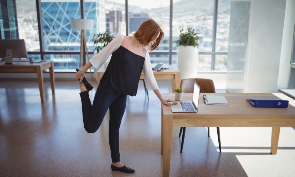 Woman performing a rear leg raise while working at her laptop
