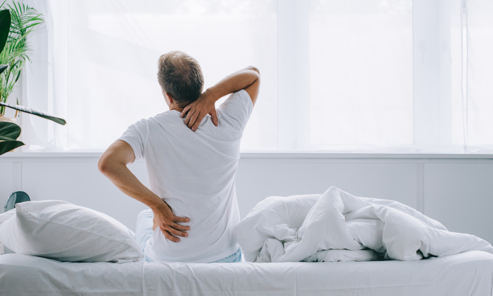 Elderly man sitting up stretching to ease back pain