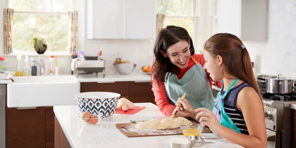 Young girl glazing bread dough with her mother in the kitchen