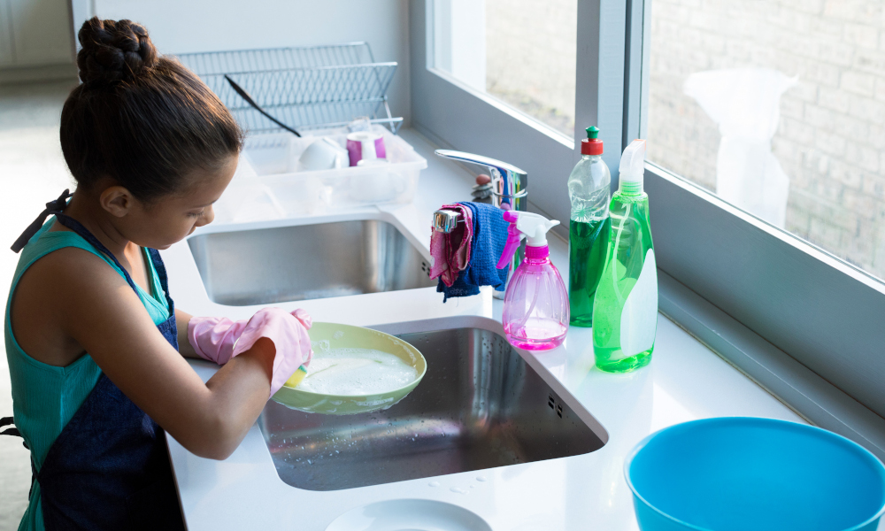 Cute little girl washing plate in kitchen sink at home