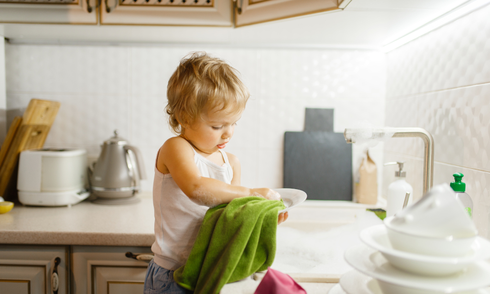 Toddler helping mother to wipe dishes with a dish towel