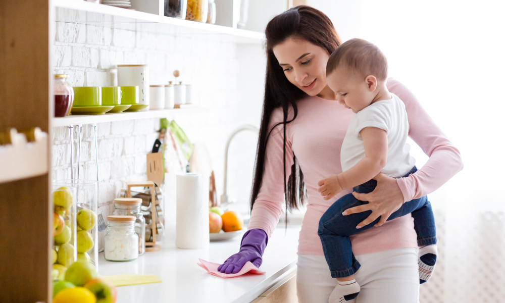 Young mother carrying a baby and cleaning the kitchen countertop