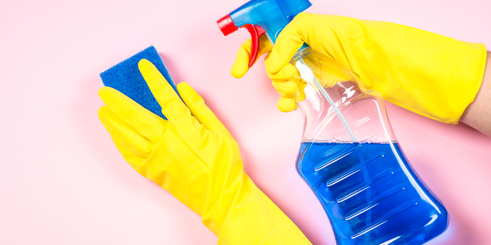 Woman cleaning pink wall with microfiber rag, gloves and cleaning spray agent.
