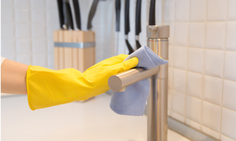 Lady in yellow rubber gloves dry the stainless steel tap with a soft cloth