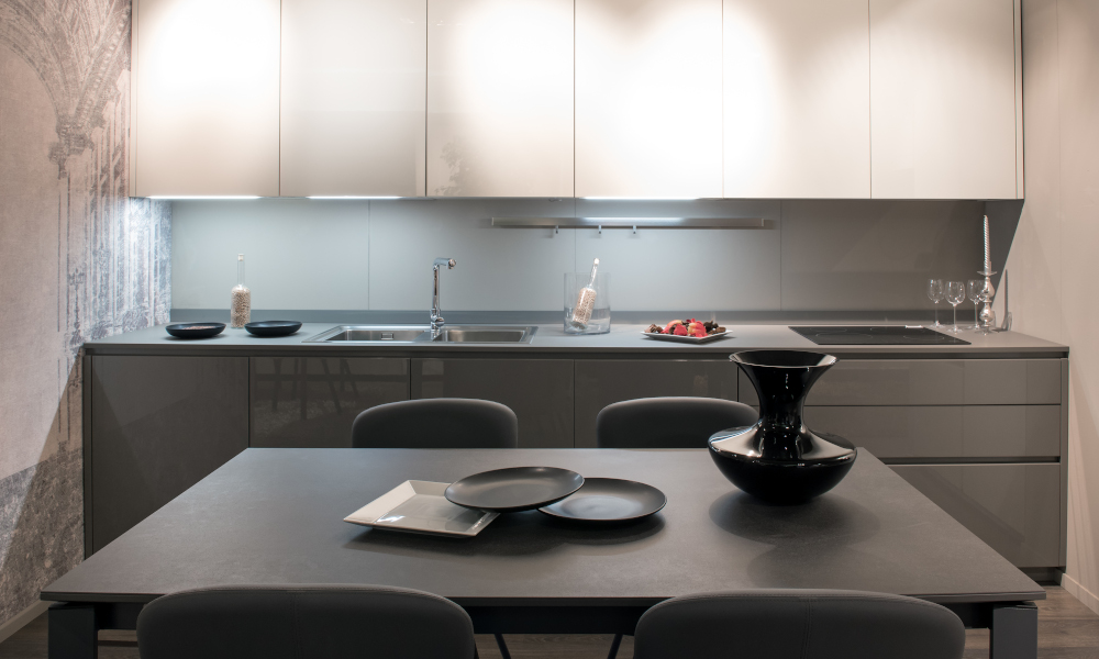 Compact modern grey and white fitted kitchen with illuminated cabinets and a dining table set with ceramics