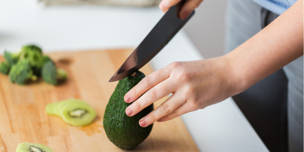 healthy eating, diet and cooking concept - close up of woman hands with knife chopping avocado on cutting board