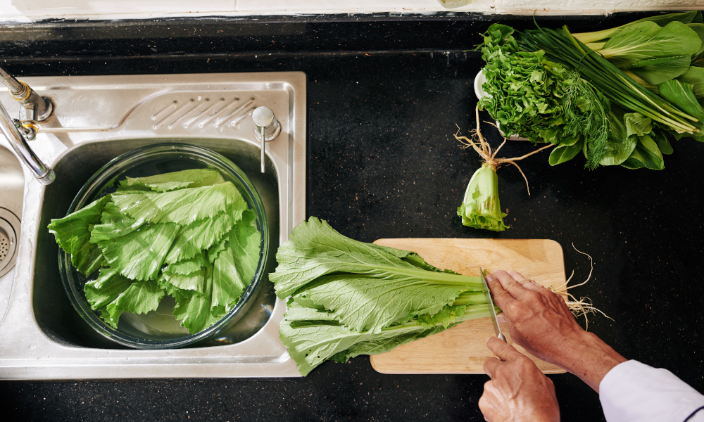 Man cutting lettuce and putting leaves in big bowl with fresh water in kitchen sink