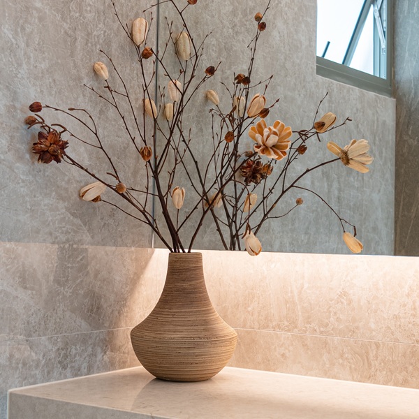 Close-up of an Aurastone vanity surface and backsplash, accented by a ceramic vase with dried flowers and soft, natural lighting.