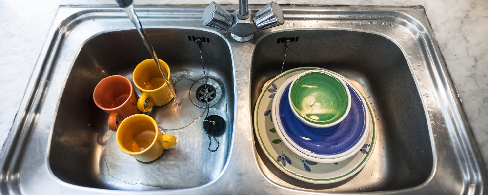 Washing dirty dishes in metallic kitchen sink at home