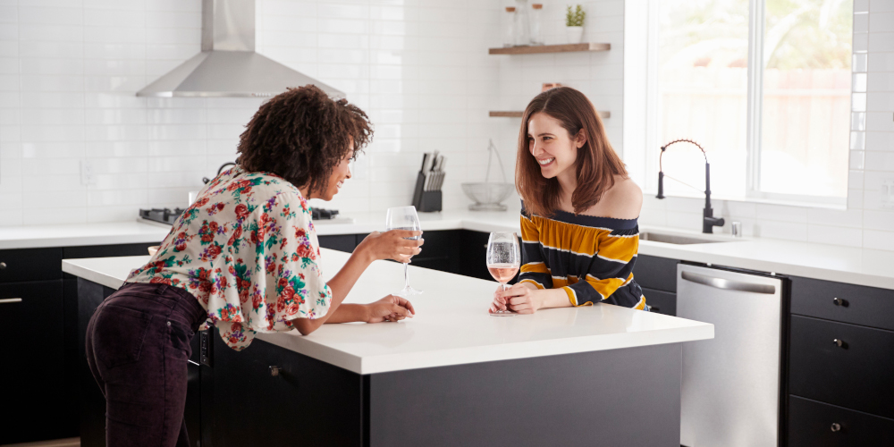 Two Female Friends Drinking Wine At Home Standing By Kitchen Island