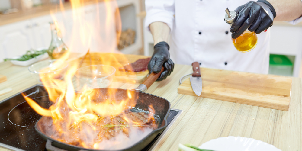 Flaming frying pan in hands of professional chef cooking in modern restaurant kitchen