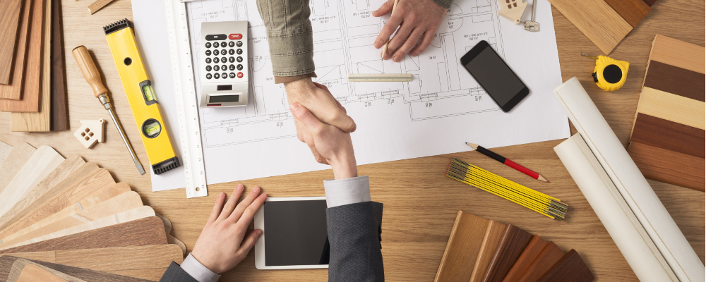 Architect and customer businessman shaking hands top view, desktop with building project, tools and wood swatches on background