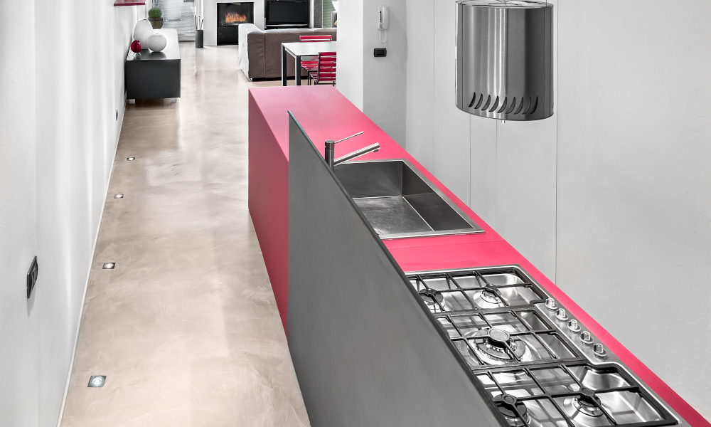 I-Shape modern kitchen interior in foreground the island kitchen with gas hob and the integrated sink on the background the living room with fireplace, the floor is made of resin