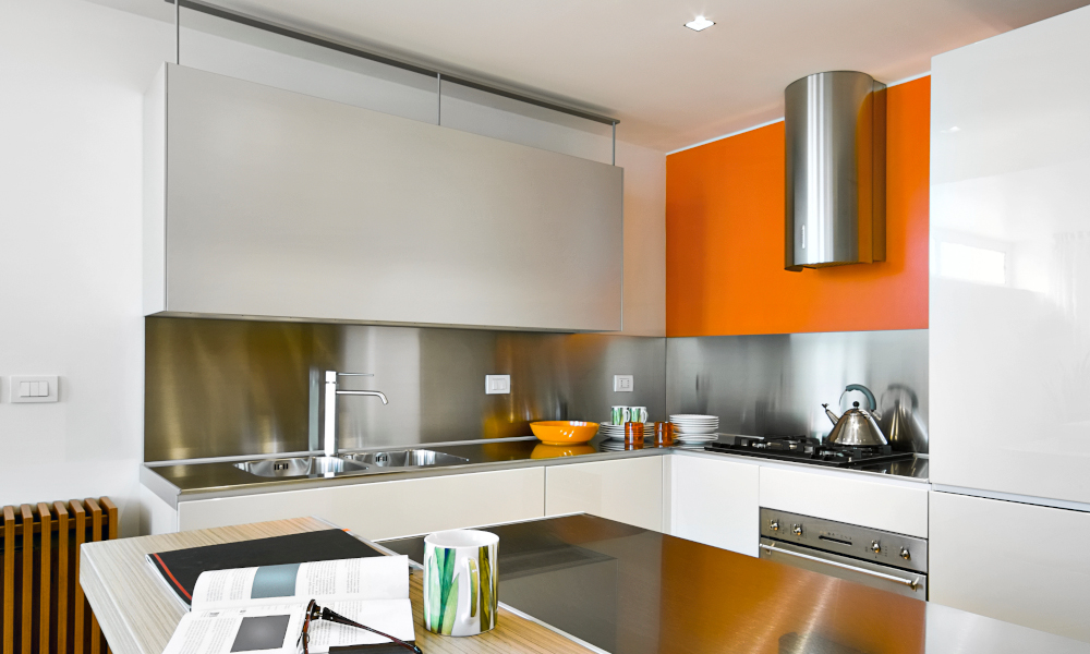 Interiors shot of a modern kitchen with orange feature cabinet, steel hood and kitchen island