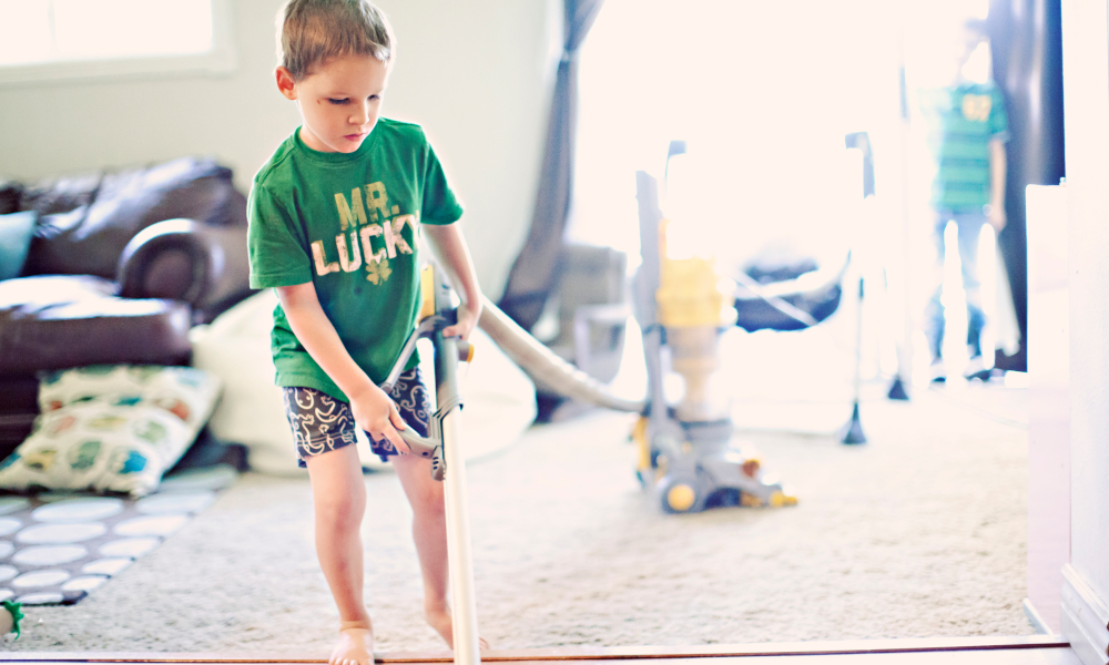 Young child helping with the household chores vacuuming the floor