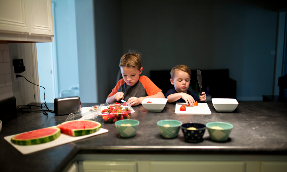 Two young boys cutting strawberries at the kitchen countertop
