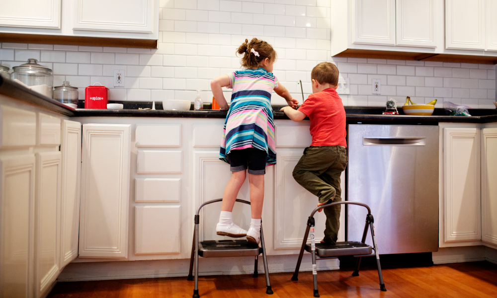 Two siblings brother and sister standing on the stool to wash the dishes