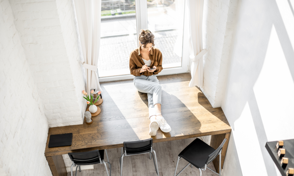 Woman sitting with phone on the huge window sill at home, view from above