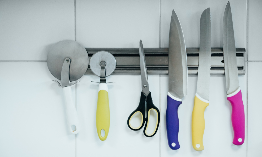 A variety of kitchen knives baker's appliances on a magnetic holder on the wall