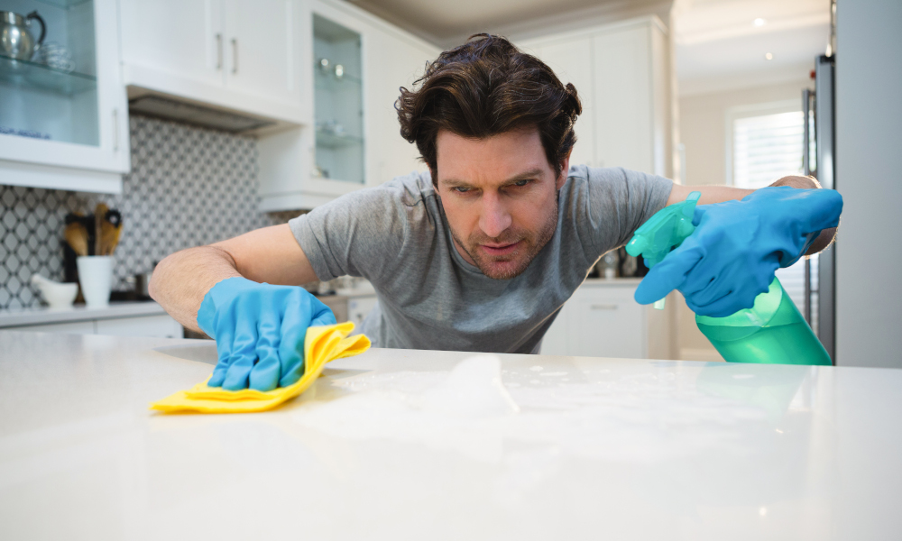 Young man sanitising the kitchen worktop at home