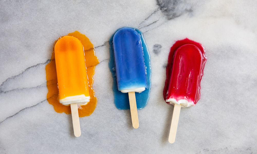Orange, blue and red popsicles melting on a marble countertop in the heat