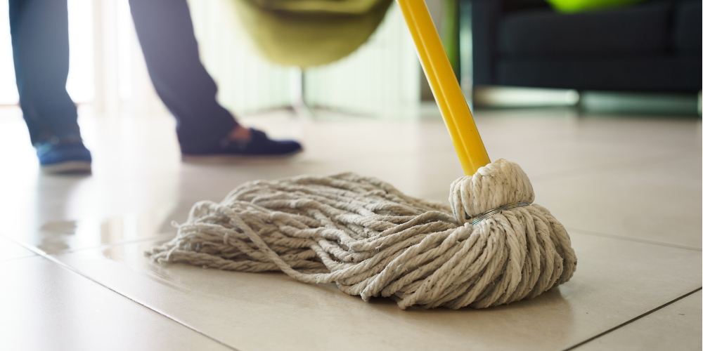 Woman at home, doing chores and housekeeping, wiping floor with water in living room. Focus on floor and mop