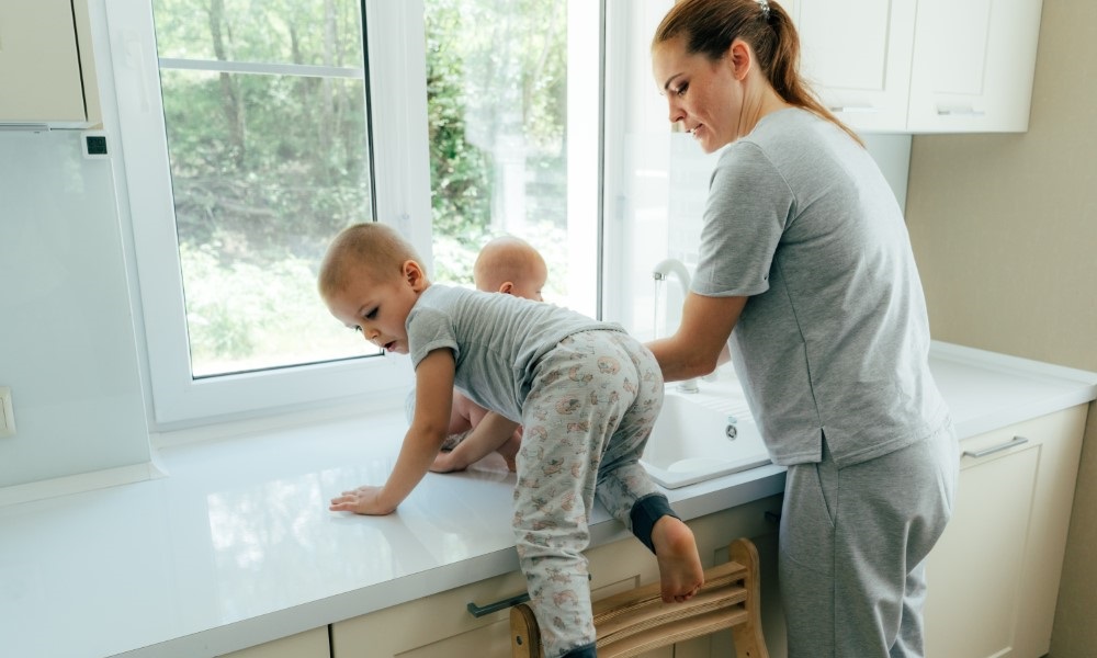Mother trying to work in the kitchen with young children climbing onto the countertop