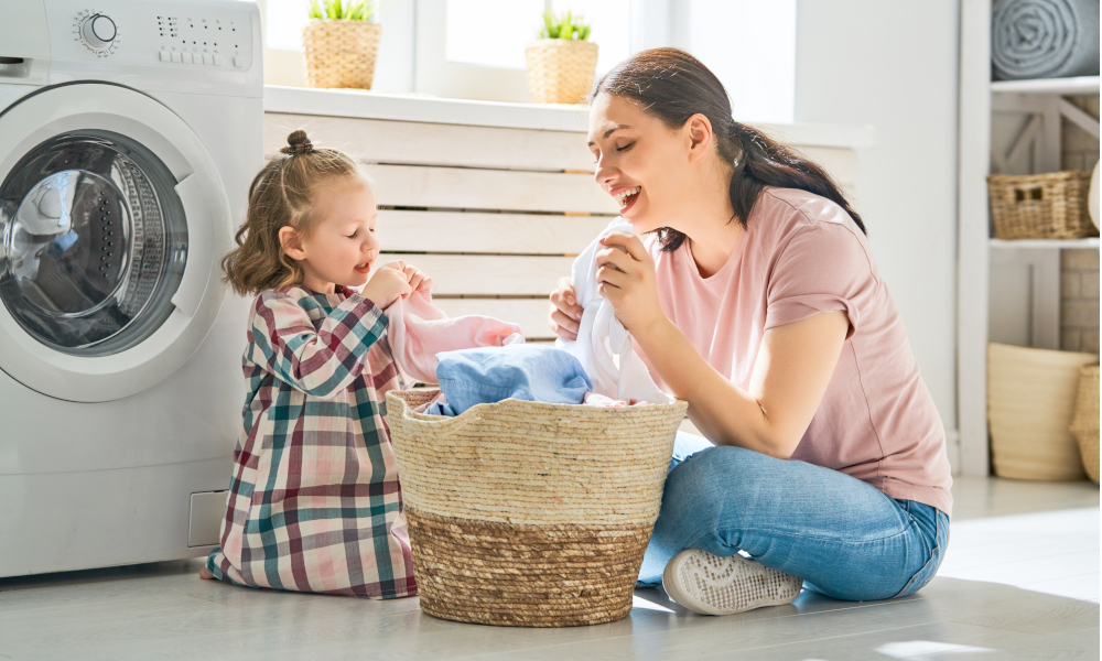 Beautiful young mother and child are having fun and smiling while doing laundry at home