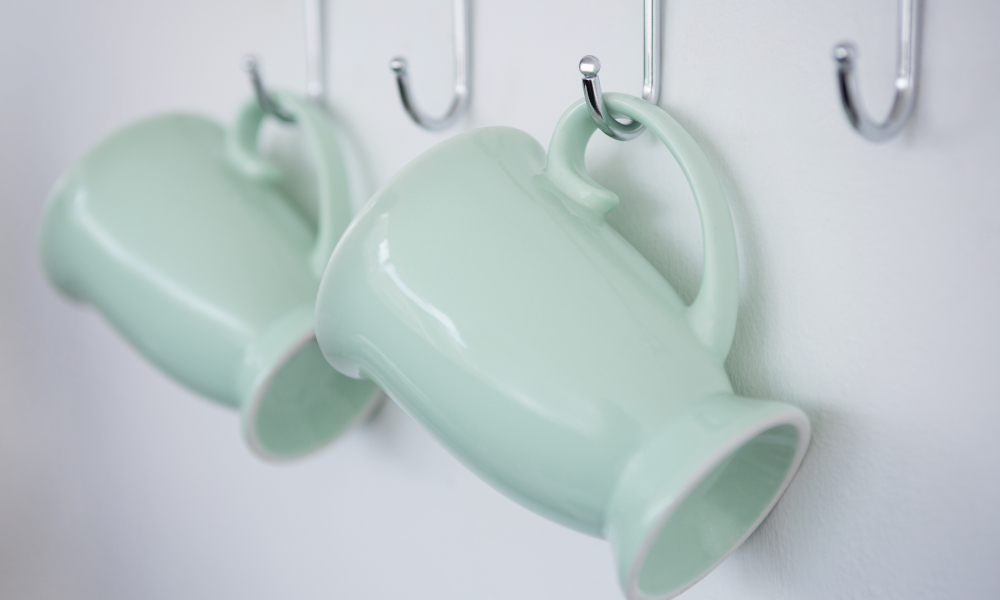 Mugs hanging on kitchen hook rail against white wall