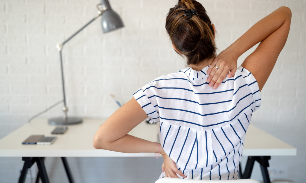 Overworked woman with back pain in office sitting on chair with bad posture