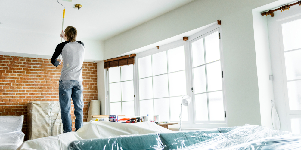 Covered furniture while man paints the living room ceiling in a major renovation