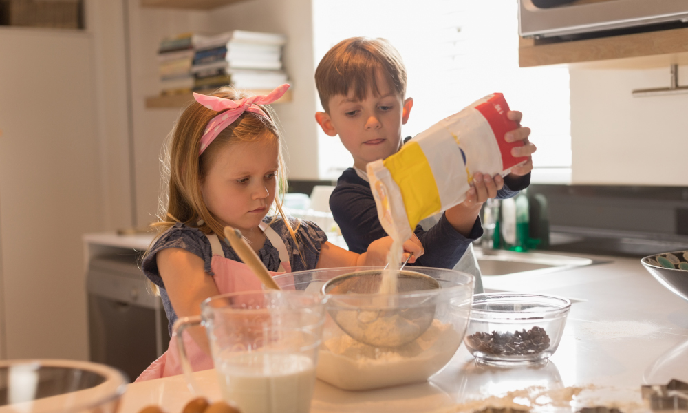 Cute siblings working together to bake cookies in modern kitchen at home