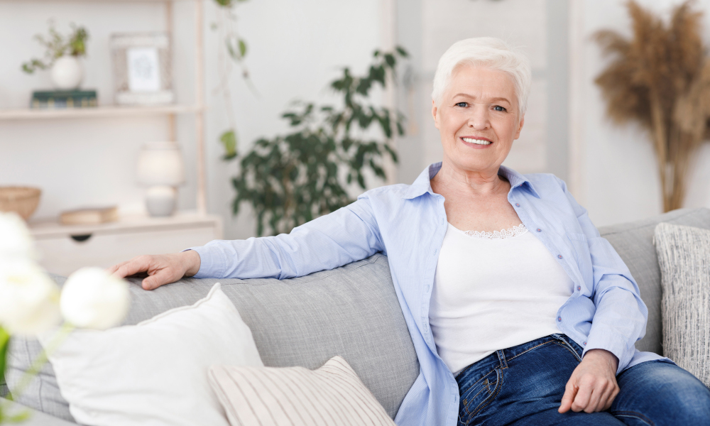 Smiling Elderly Lady Posing On Couch In Living Room At Home, Looking At Camera