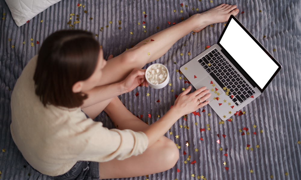 Pretty woman celebrating with her family and friends online using laptop, drinking coffee with confetti on bed