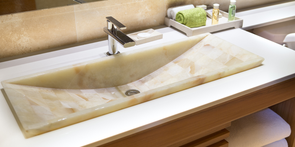 Modern marble handbasin in a hotel bathroom in a wooden vanity unit with toiletries and fresh towels