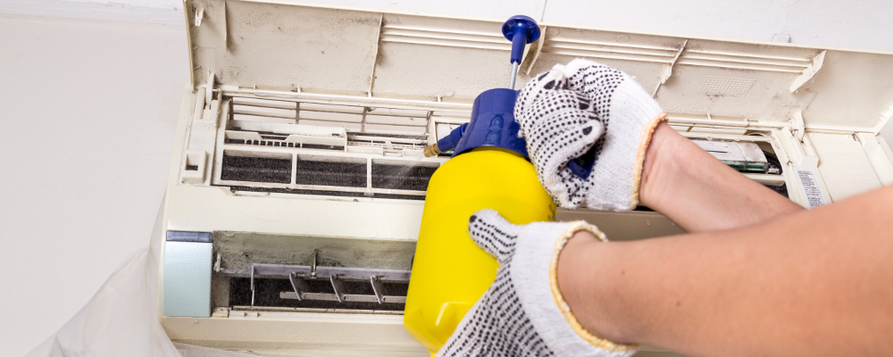 Technician spraying chemical water onto air conditioner coil to clean and disinfect air conditioner