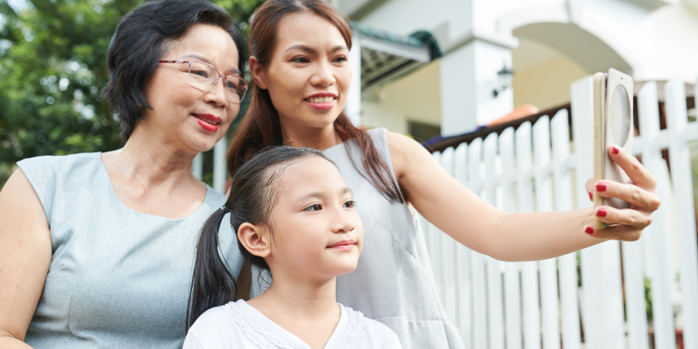 Asian family of three mother daughter and grandmother posing on mobile phone for selfie portrait while spending time outdoors