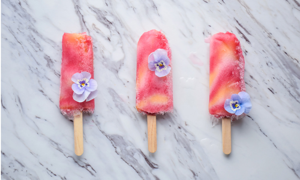 Three pink frozen popsicles with violet flowers on marble countertop