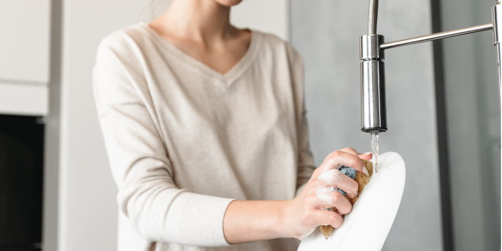 Washing dishes under running tap water in kitchen