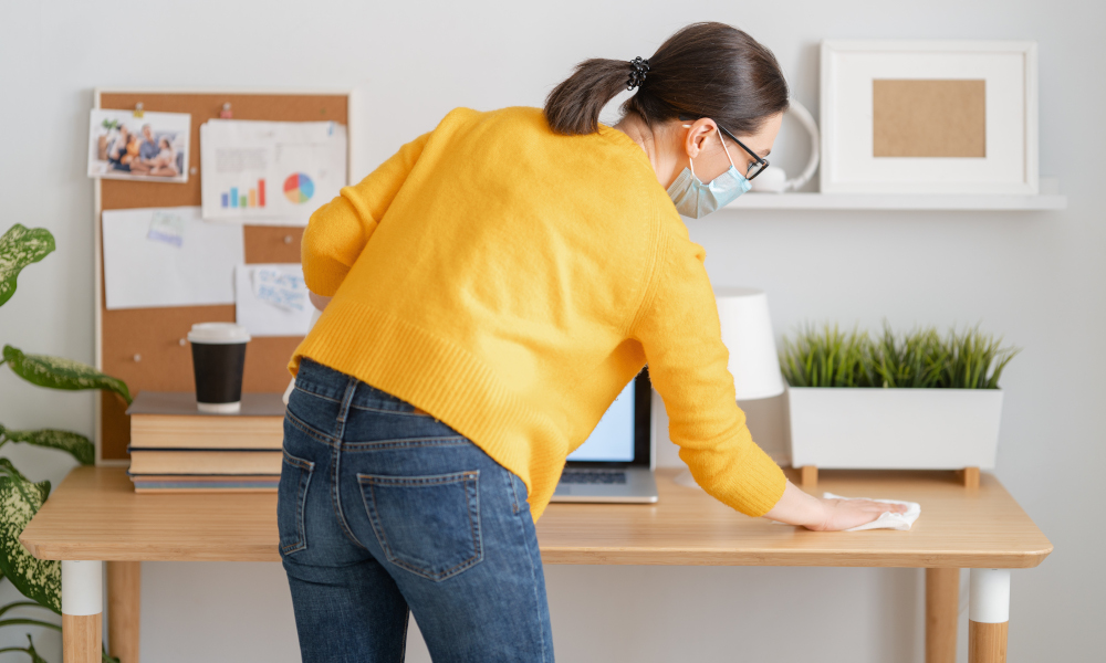 Woman in facemask cleaning her desk before working in home office