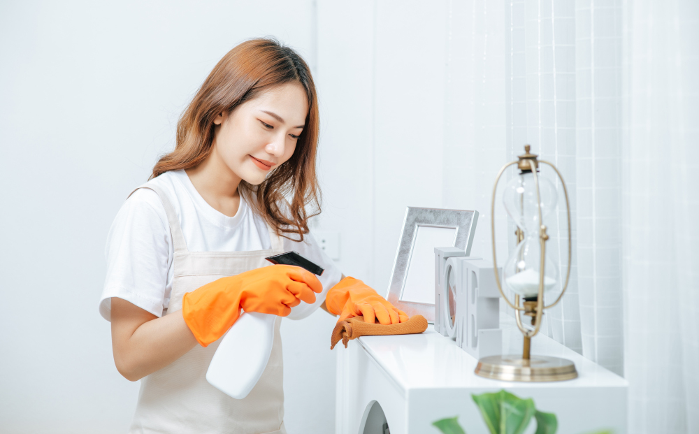 Young housekeeper woman wearing apron and rubber gloves use cleaning solution in a spray bottle on white furniture