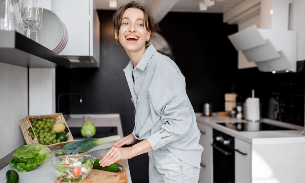 Young and cheerful woman cooking food with healthy vegetarian ingredients on the kitchen at home