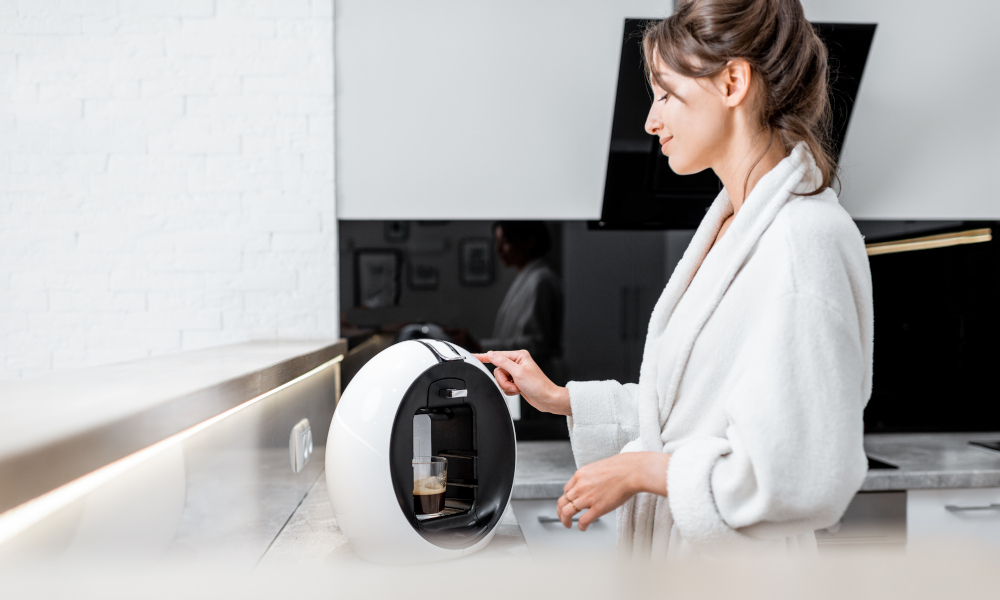 Young woman in bathrobe making coffee with a coffee machine on the kitchen countertop at home