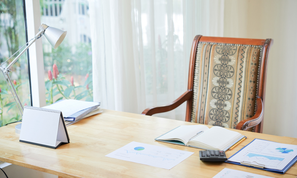 Interior shot of comfortable chair at wooden table with composed papers and notepad on desk near window