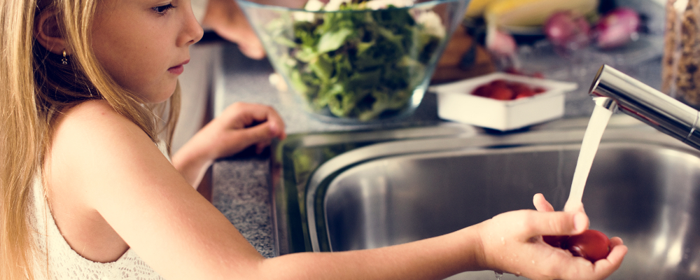 Young girl in the kitchen washing fruit at the sink