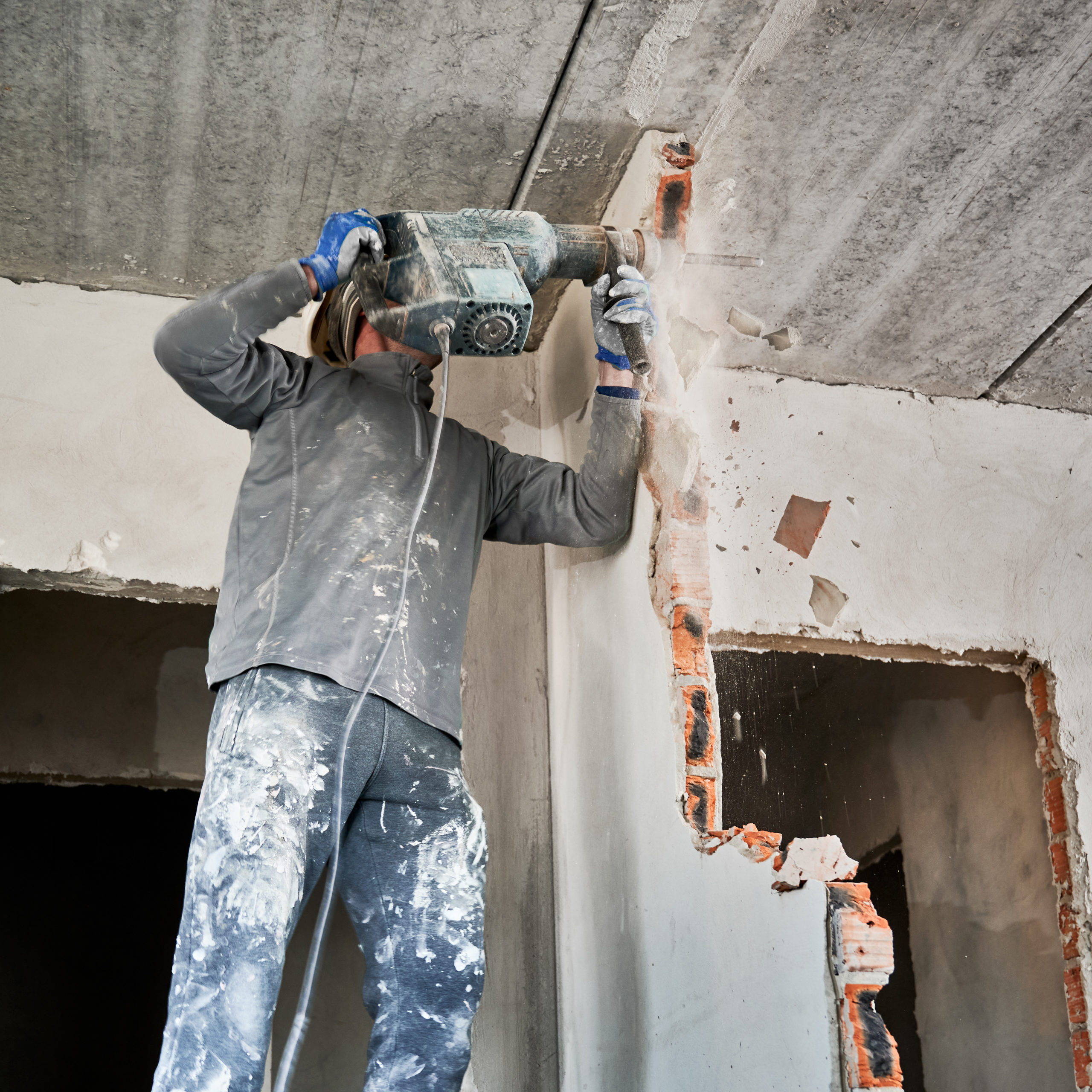 Dismantler crashing interoom wall by perforator in impact mode. Overhaul with demolition of adjacent walls to increase space of living accomodation.