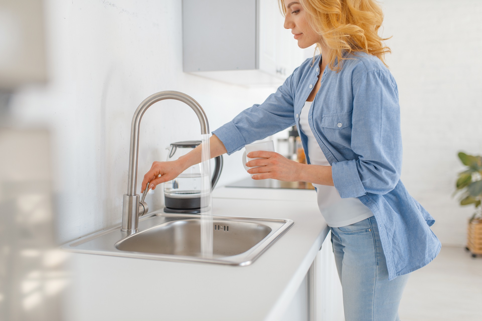 Young woman with glass at the sink on the kitchen. Female person drinks fresh water at home in the morning, healthy nutrition and lifestyle